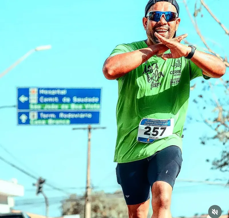 Corredor sorrindo de braços abertos numa prova de rua, céu azul